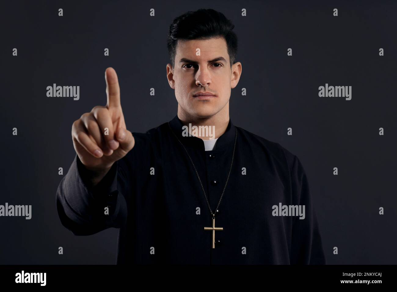 Der Priester trägt eine Soutane mit Kragen auf schwarzem Hintergrund Stockfoto