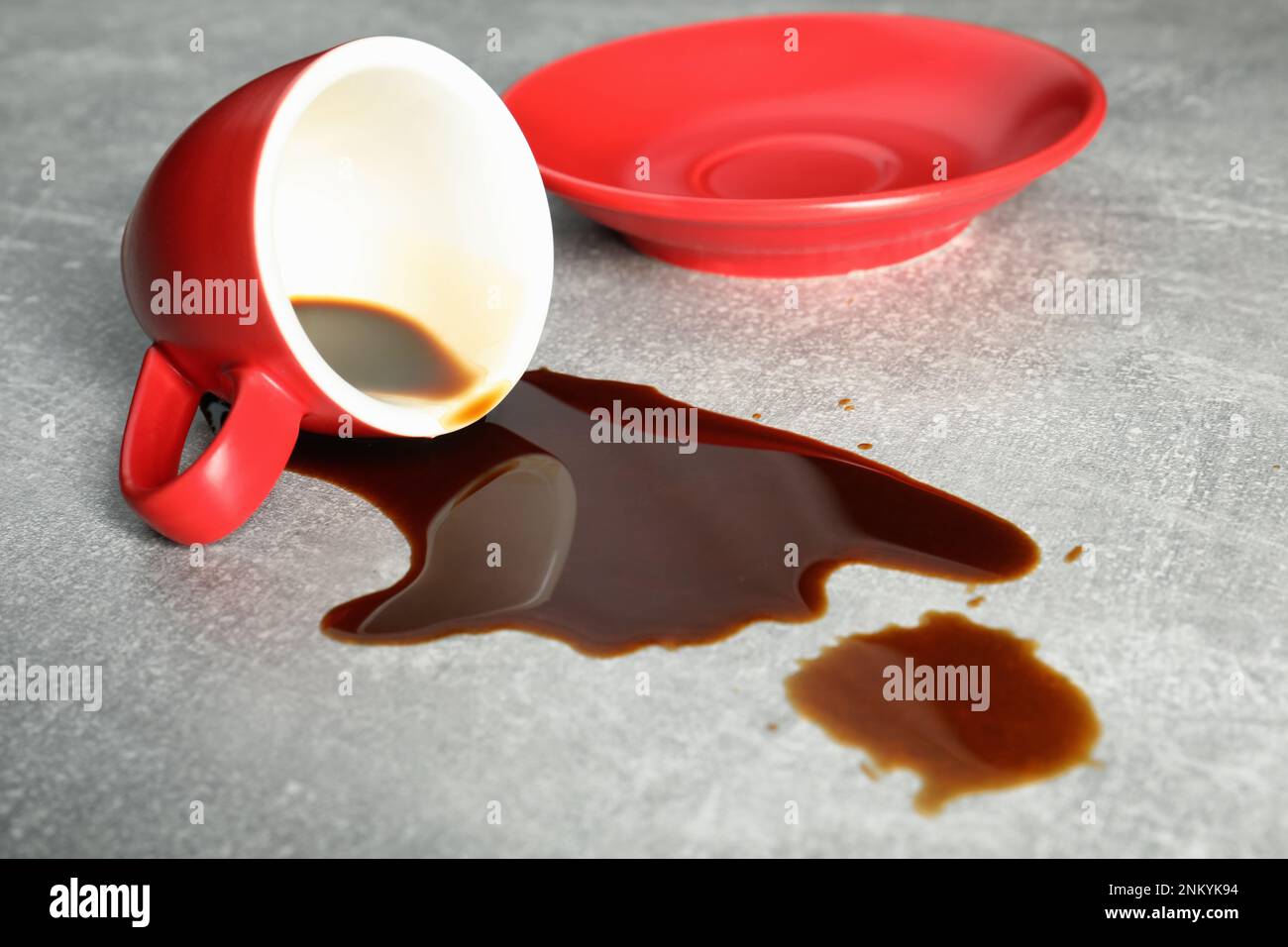 Tasse mit Untertasse und verschütteter Kaffee auf grauem Tisch Stockfoto