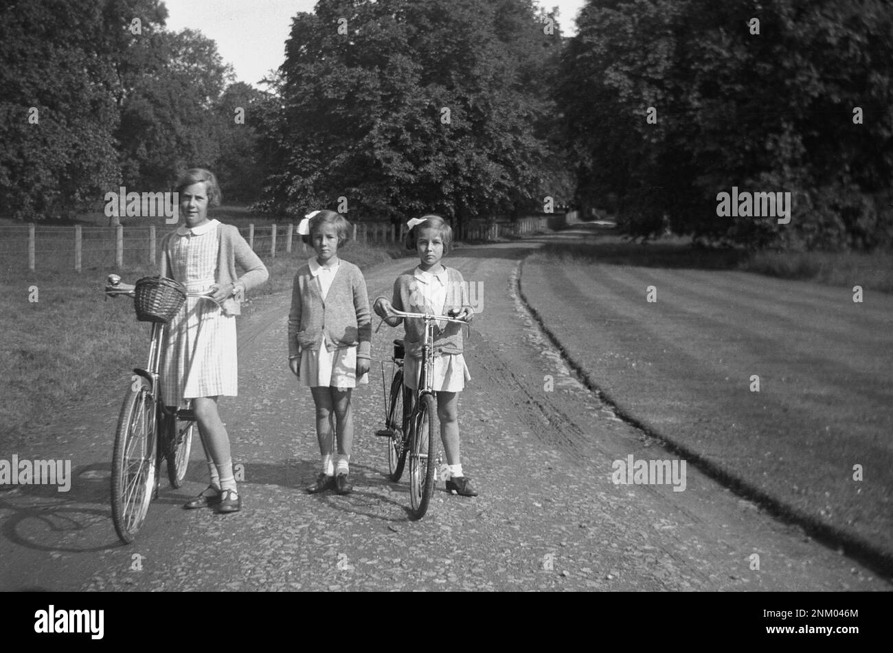 1934, historisch, nach Hause von der Schule, drei junge Schulmädchen, zwei mit ihren Fahrrädern, draußen auf einem Schotterweg eines Landbesitzes, England, Großbritannien. Stockfoto