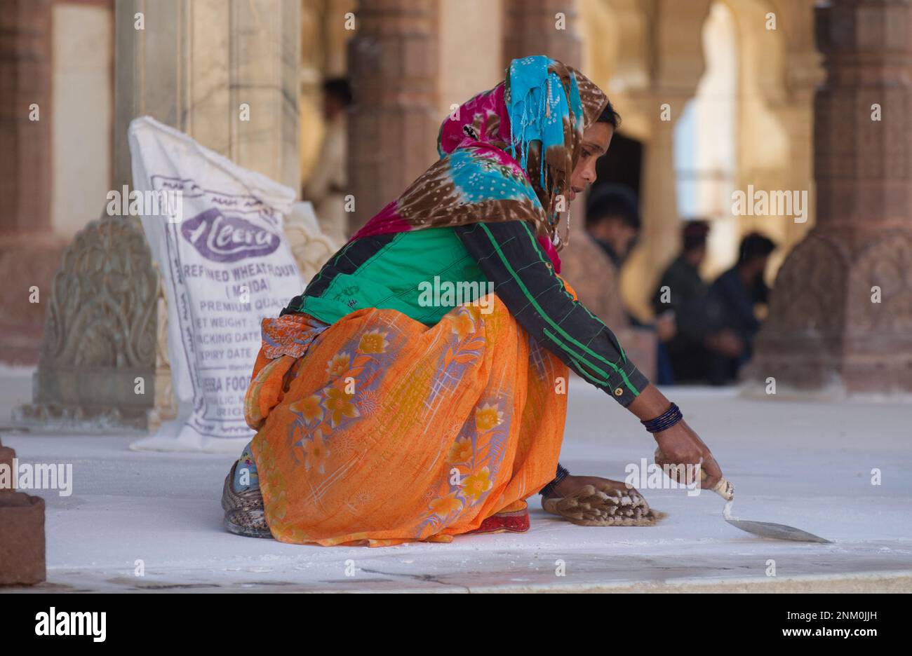 Eine indische Arbeiterin, die Reparaturen an Pflastersteinen durchführt, gekleidet in traditioneller Kleidung in schönen, leuchtenden Farben. Ein Bild von Stärke und Schönheit Stockfoto