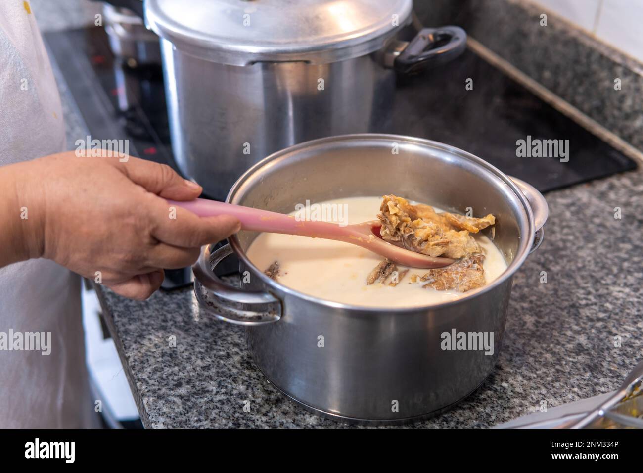 Rühren Sie gesalzenen Kabeljau von Hand aus dem Topf, indem Sie das Salz mit Milch entfernen Stockfoto