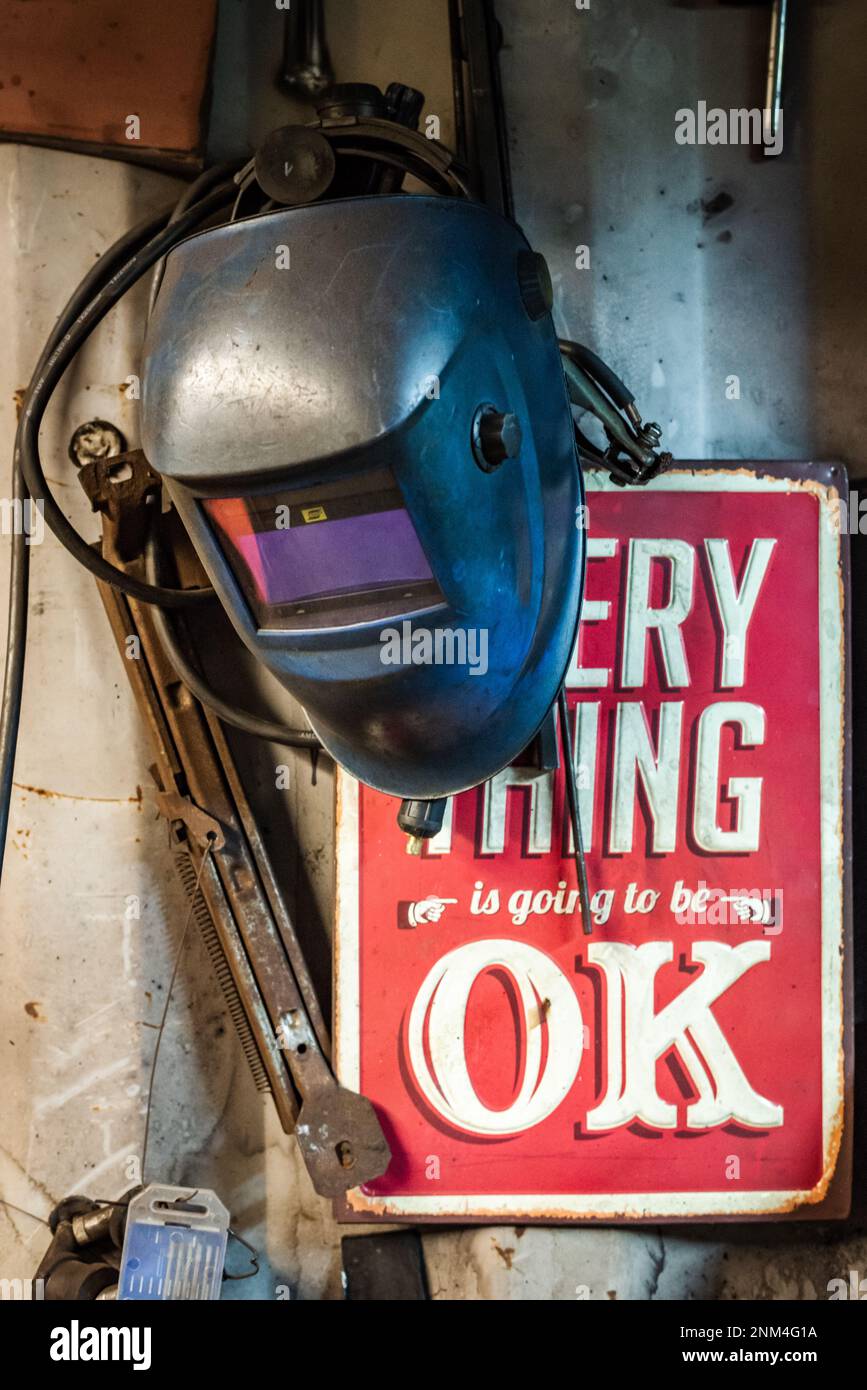 Schweißmaske hängt an der Wand vor einem roten Schild in einer Werkstatt Stockfoto