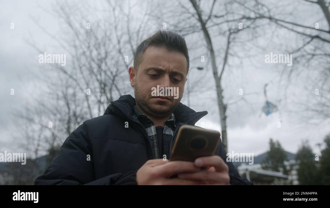 Mann mit schöner Haut und kurzem Haar lächelt, während er sein Smartphone für Textnachrichten oder Online-Zahlungen im Freien nutzt Stockfoto Mann mit schöner Haut und kurzem Haar lächelt, während er sein Smartphone für Textnachrichten oder Online-Zahlungen im Freien nutzt Stockfoto