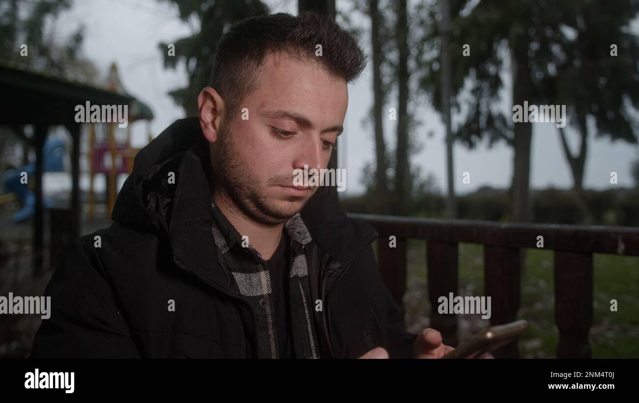 Ein Mann mit kurzen Haaren, der lacht und am Telefon im Park SMS schreibt Stockfoto