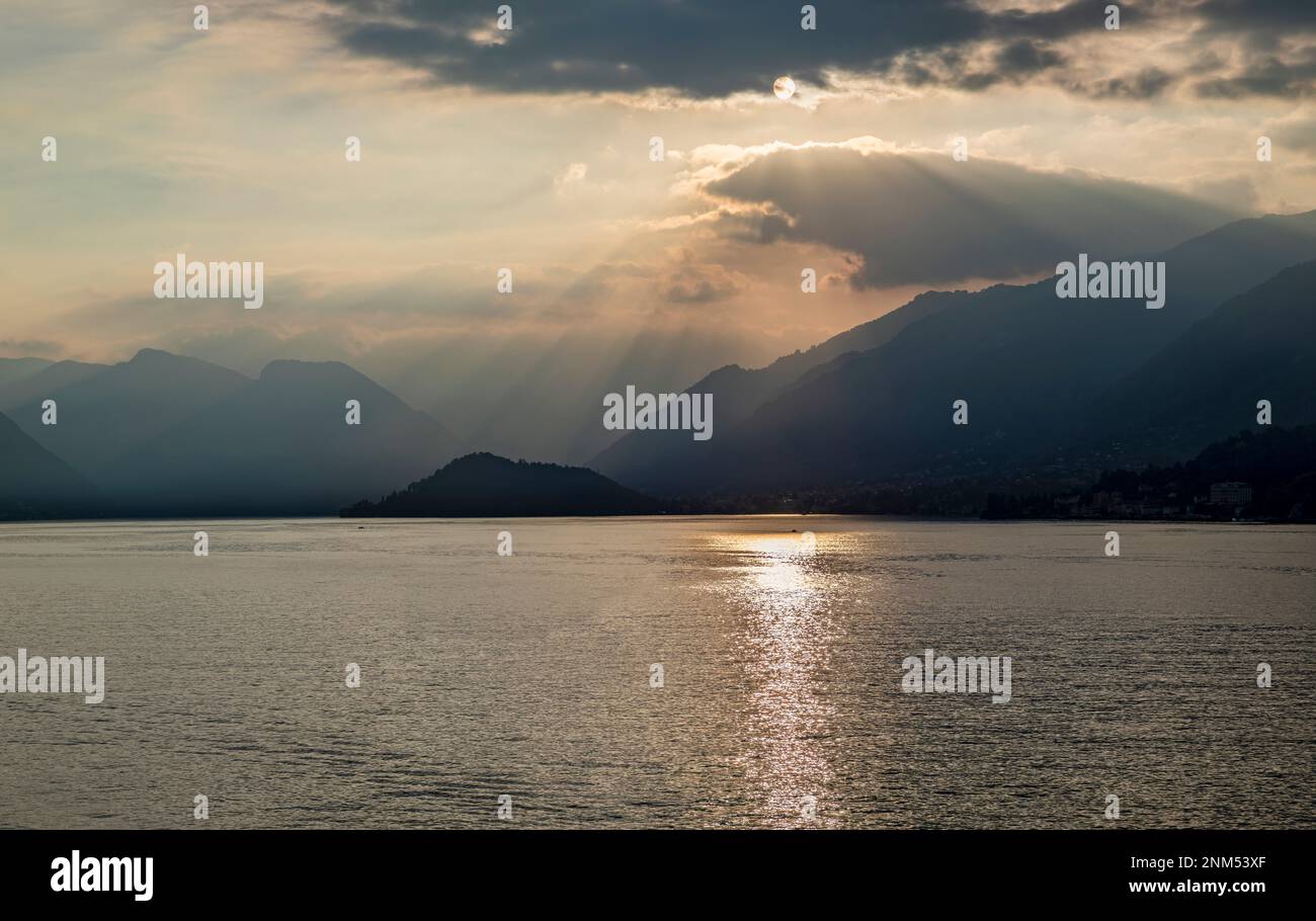 Am späten Abend im Sommer am comer See mit trüben Bergen und Sonnenstrahlen, die durch die Wolken scheinen Stockfoto