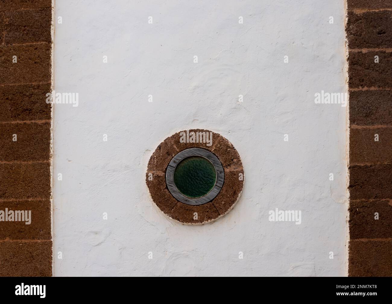 Weiße, strukturierte Fassade einer historischen Kirche. Linien mit braun-orangefarbenen Details und einem kreisförmigen Fenster. Antigua, Fuerteventura, Kanarische Inseln Stockfoto