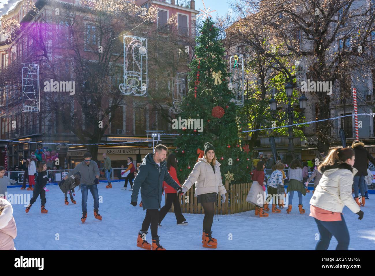 Granada, Spanien; 18. Dezember 2022: Schlittschuhlaufen von Erwachsenen und Kindern auf einer Eisbahn neben einem Weihnachtsbaum an einem sonnigen Wintermorgen in Granada (Spanien) Stockfoto