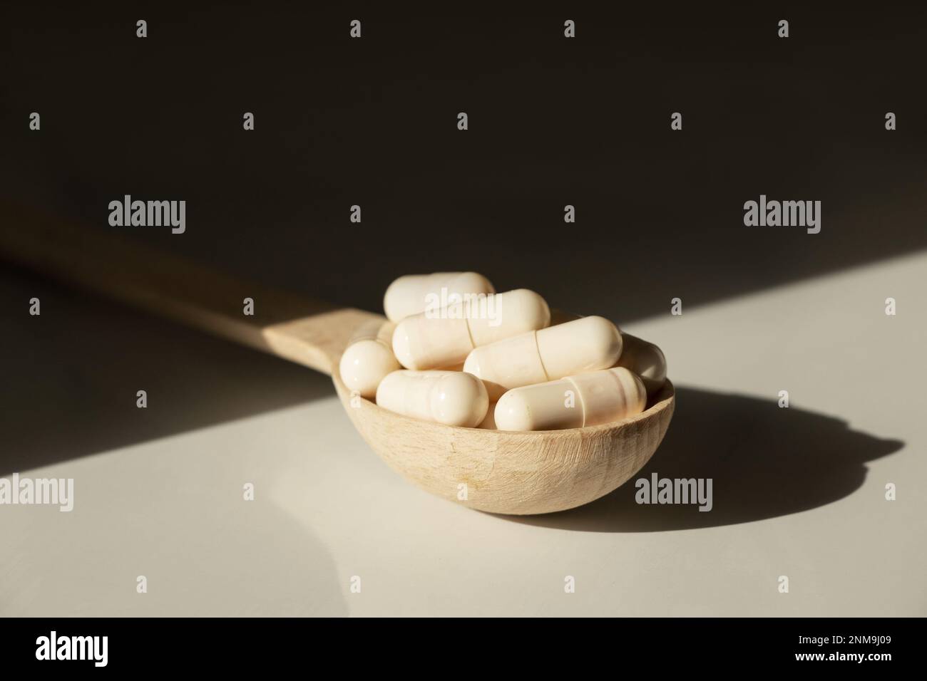 Pillen in einem Holzlöffel auf einem Tisch in der Sonne, Medikamente und Vitamine Stockfoto