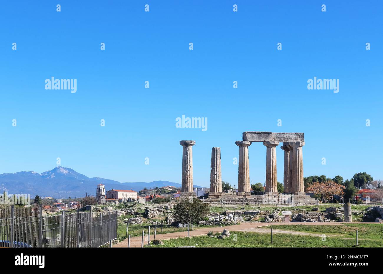 Die Ruinen des Apollotempels im antiken Korith Griechenland mit einer Kirche und einem Dorf und hohen Bergen im Hintergrund Stockfoto