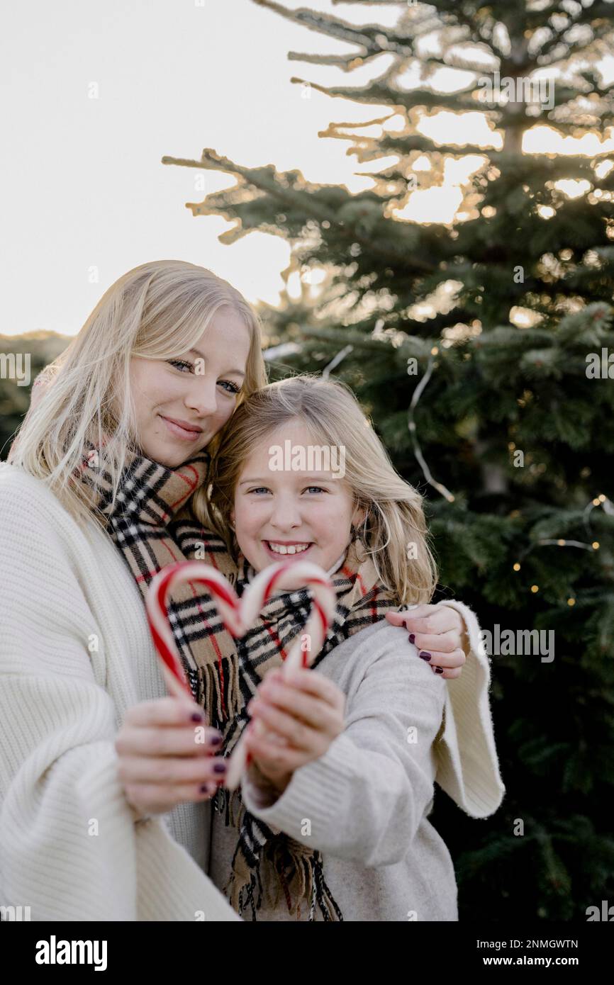 Zwei Mädchen mit Zuckerstangenherzen vor einem Weihnachtsbaum Stockfoto