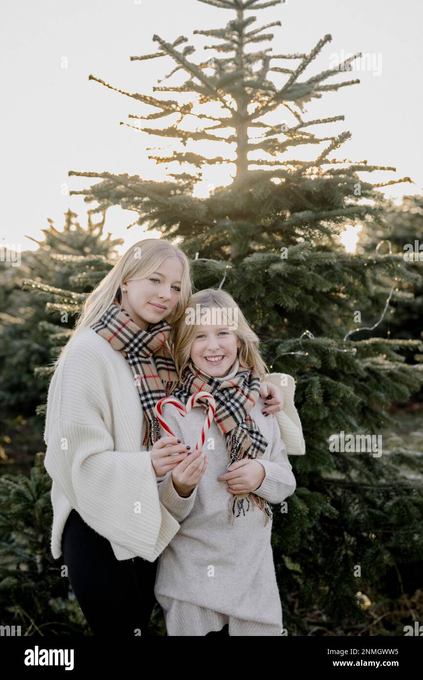 Zwei Mädchen mit Zuckerstangenherzen vor einem Weihnachtsbaum Stockfoto