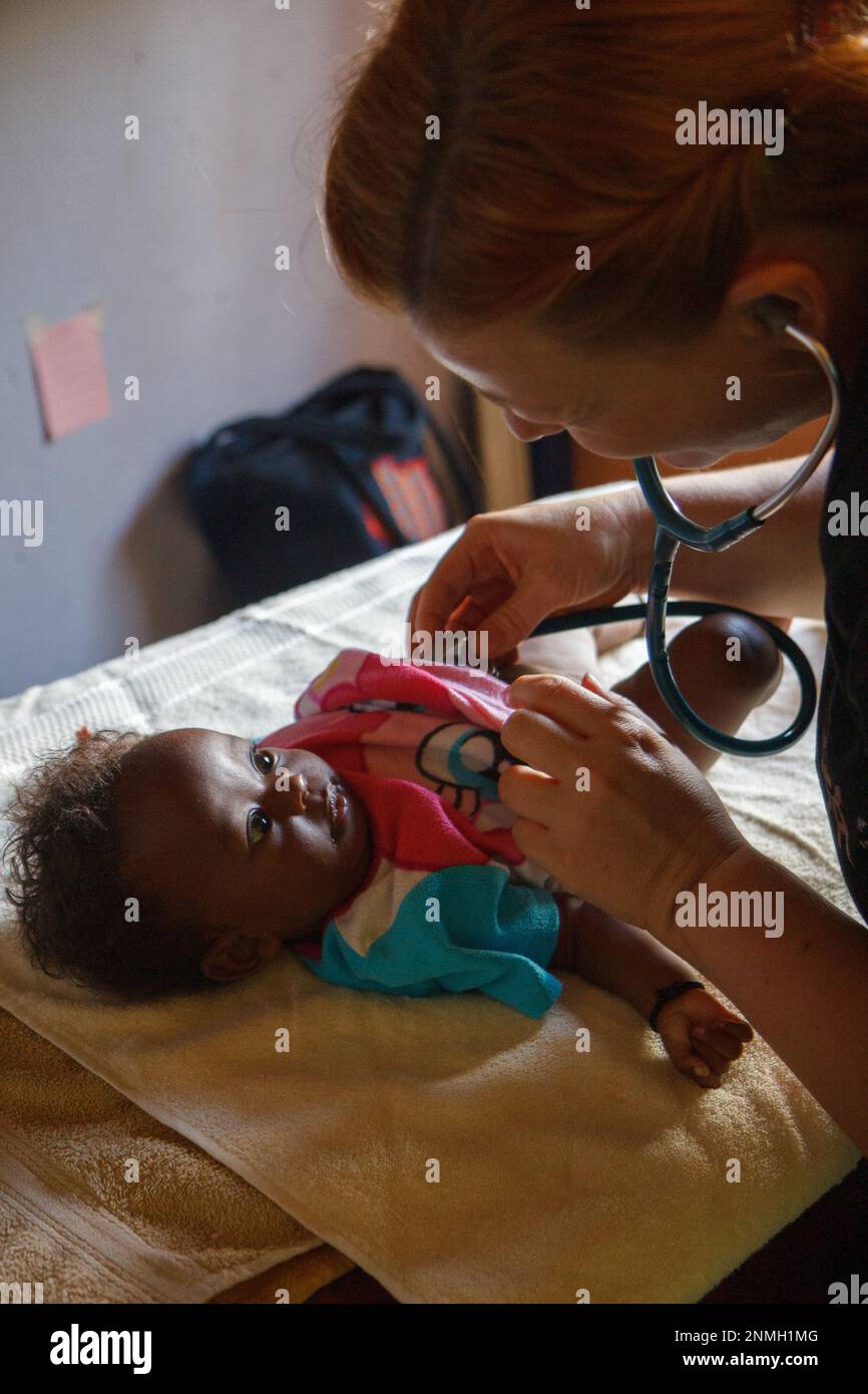 Ein weißer Arzt untersucht ein schwarzes Baby mit einem Stethoskop. Stockfoto