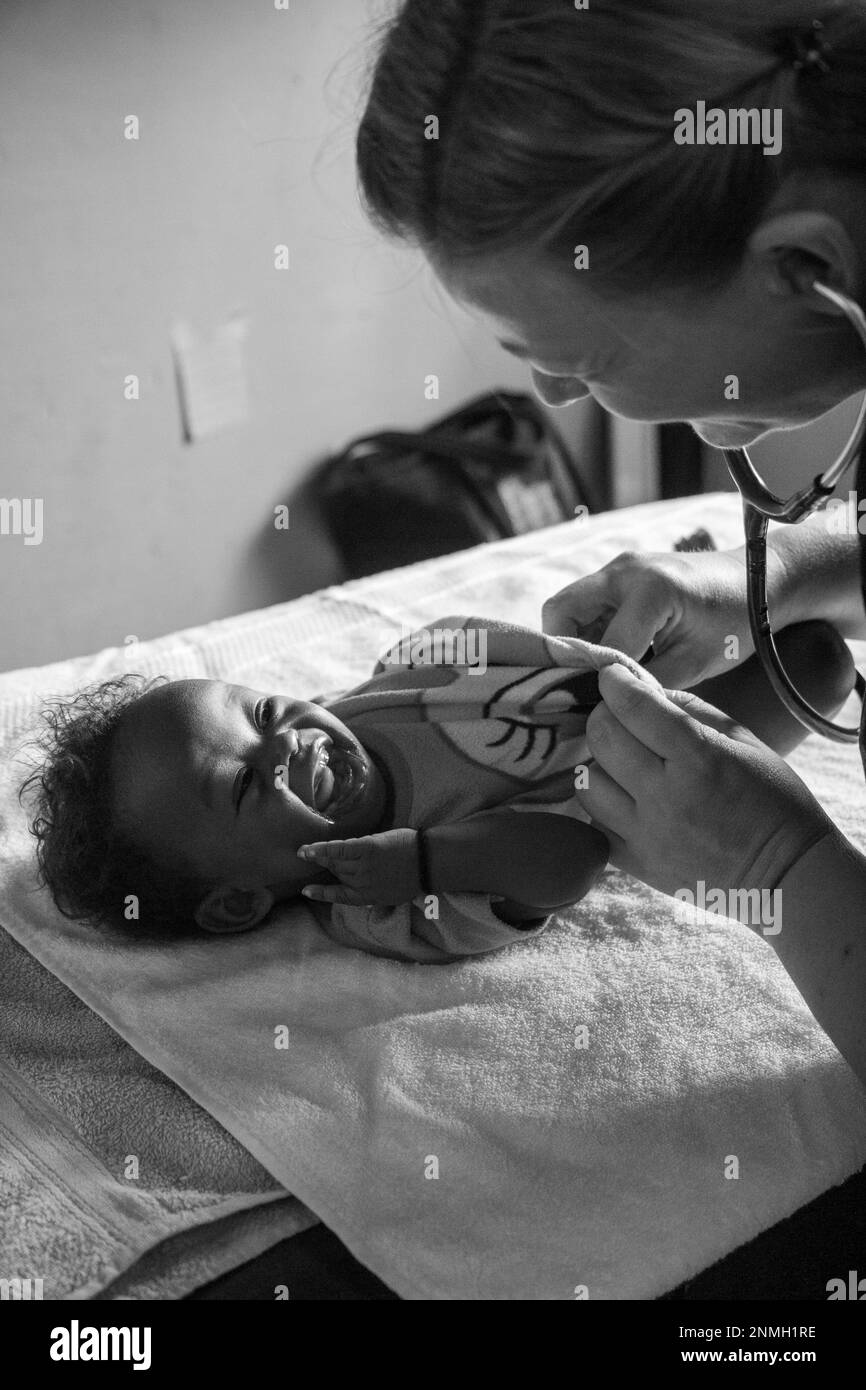 Ein weißer Arzt untersucht ein schwarzes Baby mit einem Stethoskop. Stockfoto
