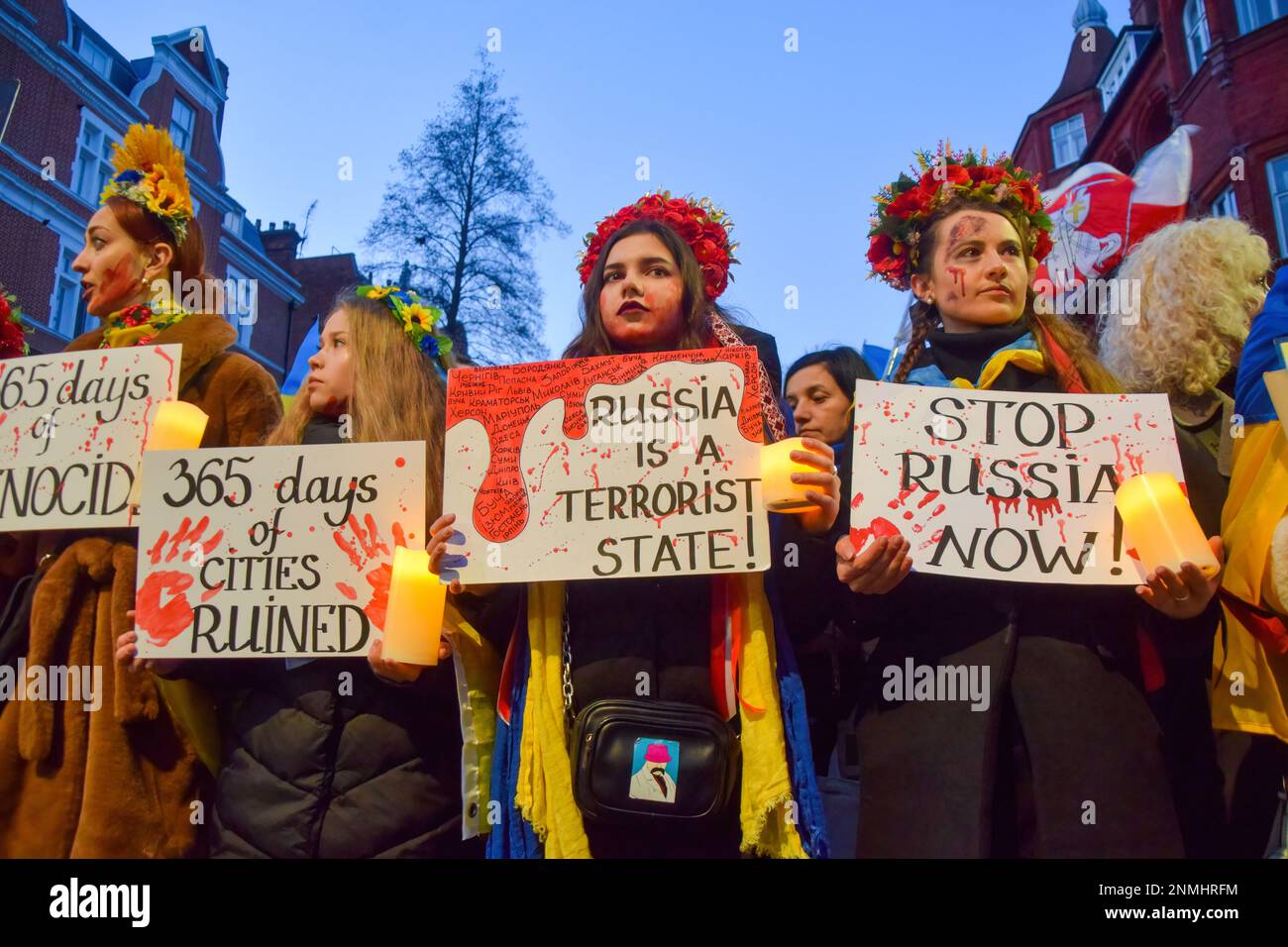 London, Großbritannien. 24. Februar 2023. Demonstranten mit Blumenkopfschmuck halten während der Demonstration außerhalb der russischen Botschaft Kerzen und antirussische Plakate. Tausende von Menschen marschierten aus Holland Park in die russische Botschaft während eines Protestes gegen die Ukraine am ersten Jahrestag der russischen Invasion. Kredit: SOPA Images Limited/Alamy Live News Stockfoto