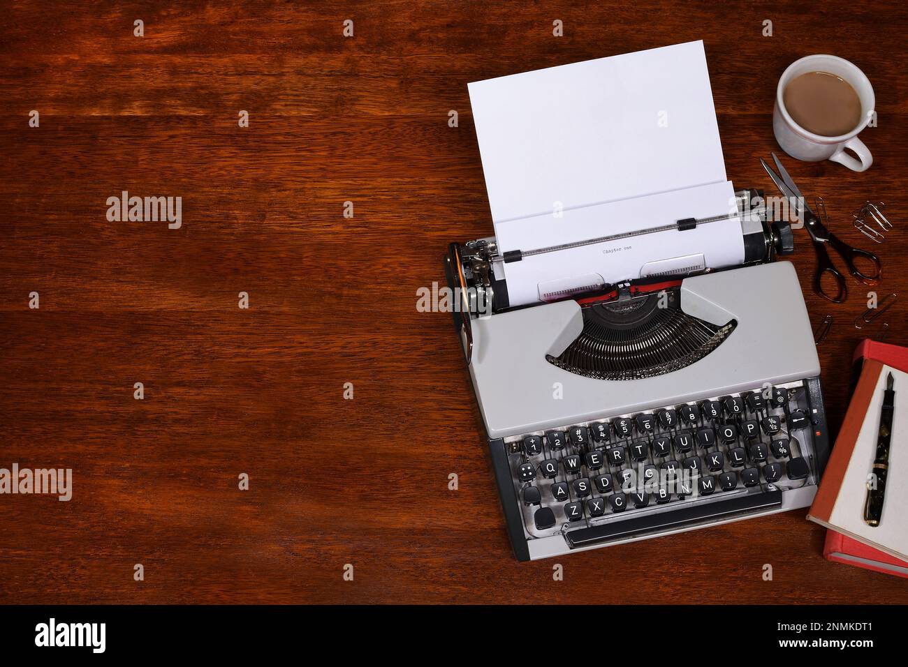 Eine flache Draufsicht auf eine Schreibmaschine aus den frühen 60er Jahren auf einem dunkelbraunen Schreibtisch, mit Büchern, Füllfederhalter und Kaffeetasse und Kopierbereich auf der linken Seite Stockfoto