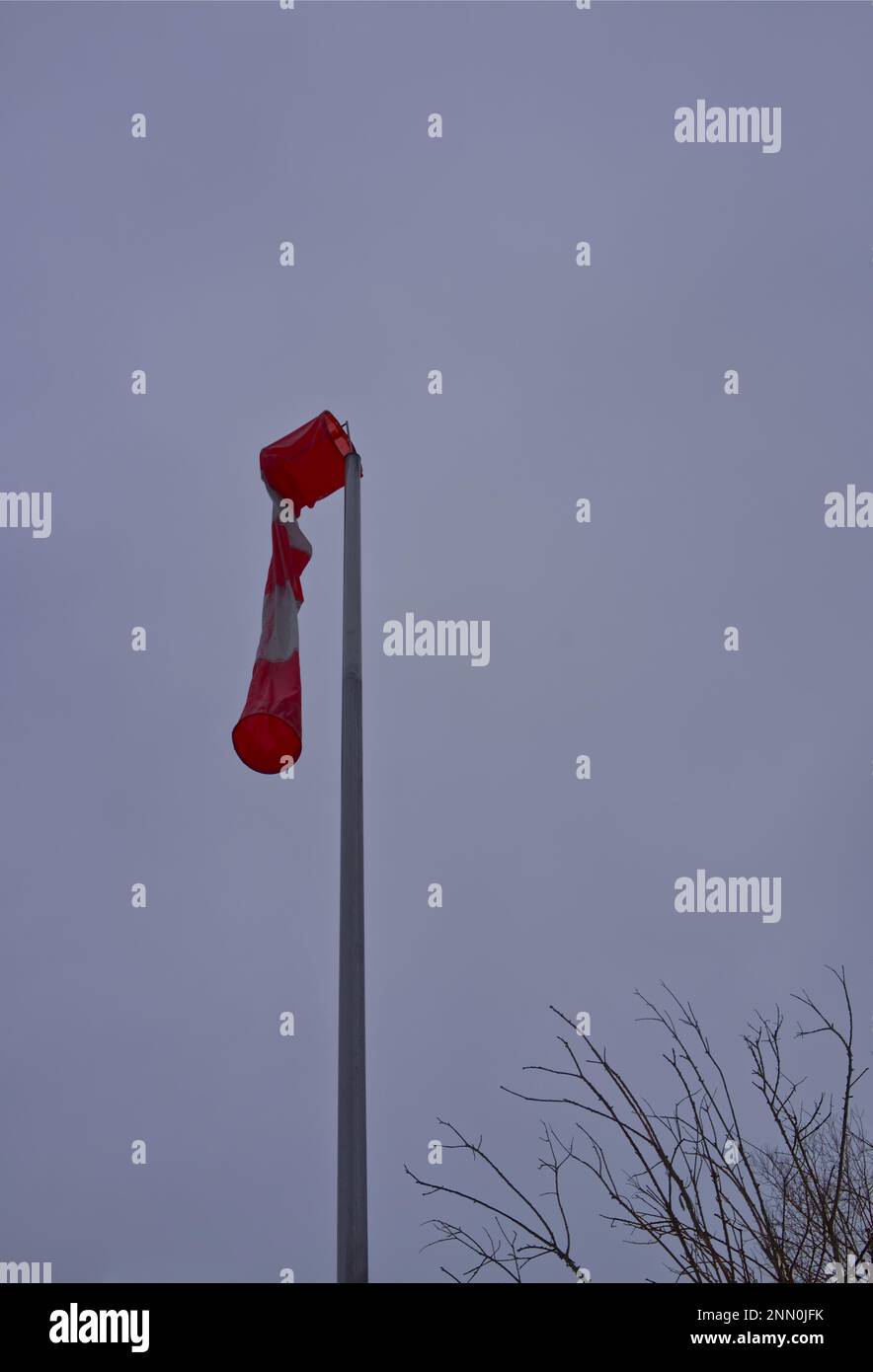 Eine Windsocke in rot-weißen Streifen in hängender Position an einem Laternenpfahl, die einen Windmangel signalisiert (möglicherweise die Windstille vor dem Sturm) Stockfoto