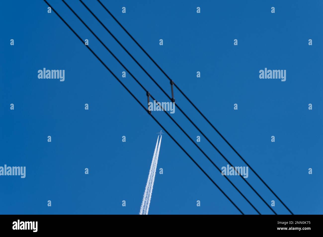 Ein Flugzeug in klarem blauem Himmel mit seinem Kontrast, der scheinbar eine Reihe von Stromkabeln überquert Stockfoto