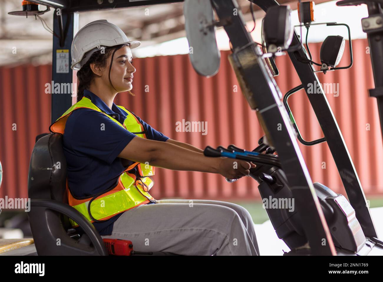 Indische Mitarbeiterin arbeitet Gabelstaplerfahrer auf dem Containerplatz des Hafenlagers für die Logistikindustrie, fröhliches Lächeln Stockfoto