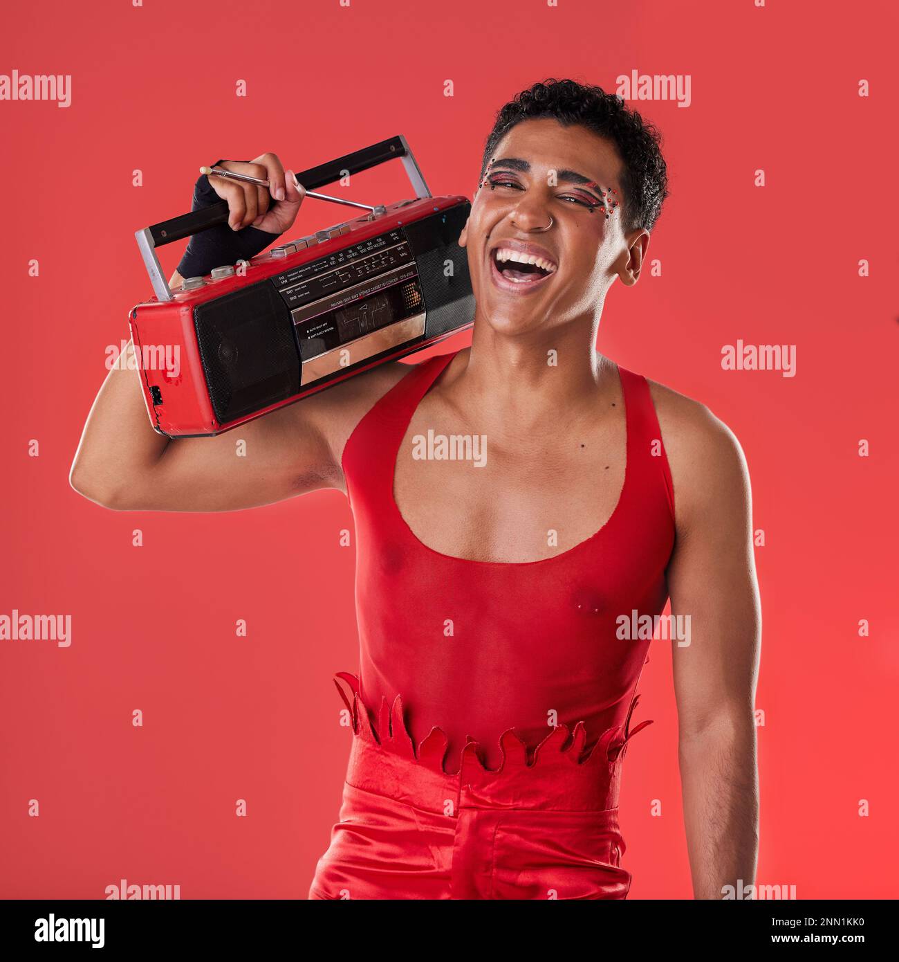 Happy, man und Boombox-Radio im Studio für schwule, stolze und vogue-Ästhetik mit Retro-80s-Technologie auf rotem Hintergrund. LGBTQ-Modell, Vintage-Mode und Stockfoto