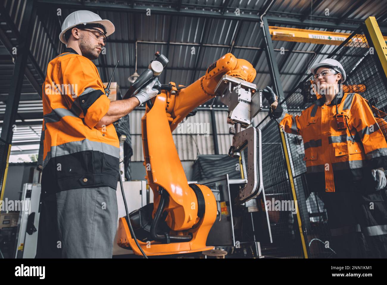 Ingenieurteam Service Roboterschweißen in Automatisierungsfabrik. Mitarbeiter im Sicherheitsanzug arbeiten an der Programmierung oder dem Austausch von PAR-Software für Roboterarme Stockfoto