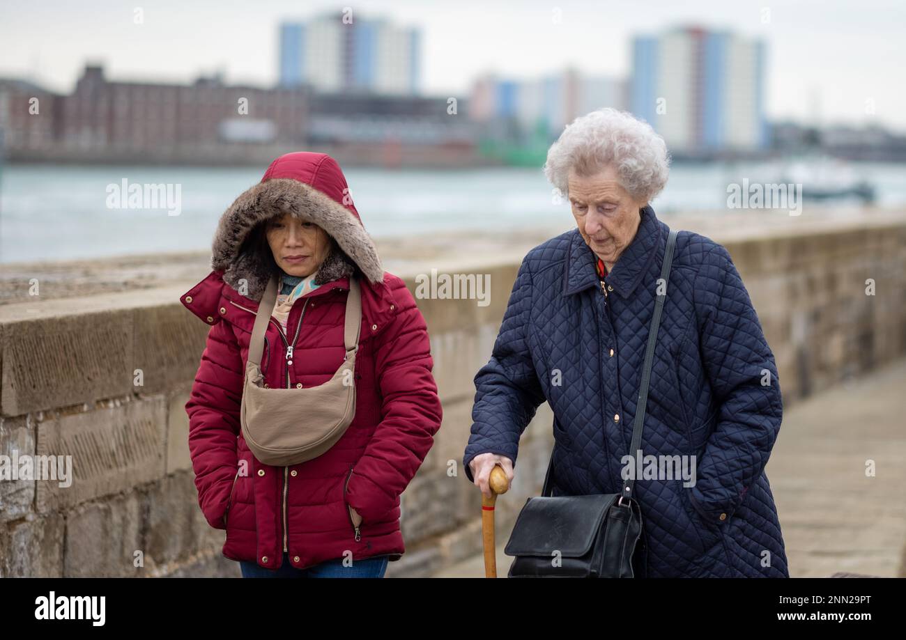 Eine 92-jährige Frau verwendet einen Gehstock, wenn sie mit ihrer vietnamesischen Schwiegertochter am Hafen von Portsmouth in Großbritannien entlang spaziert. Stockfoto