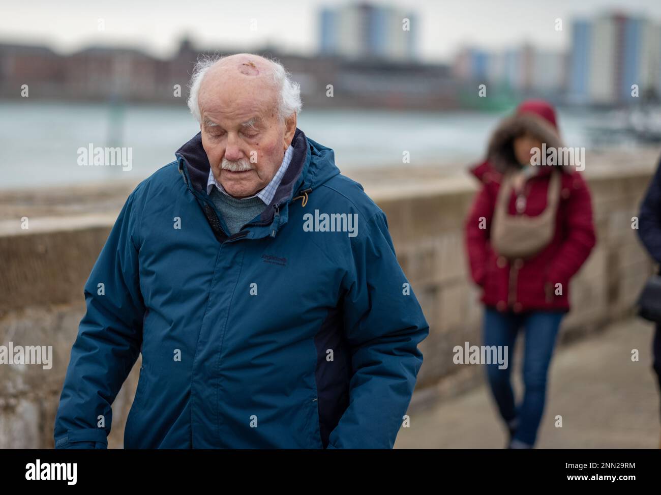 Ein 96-jähriger Mann blickt nach unten, während er vorsichtig entlang der Ufermauer in Portsmouth Harbour, Großbritannien, geht. Stockfoto