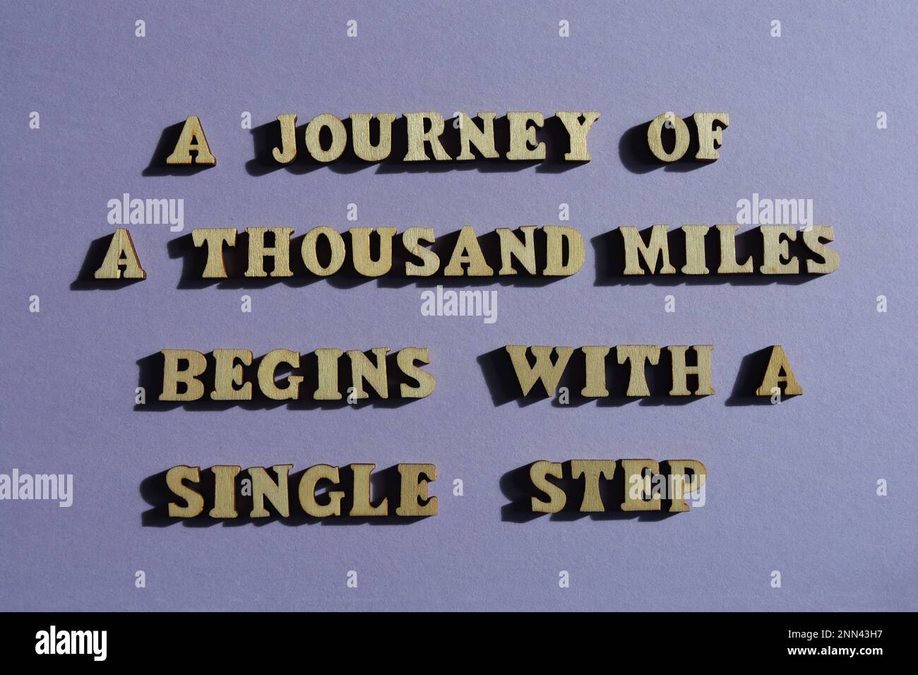 Eine Reise von tausend Meilen beginnt mit einem einzelnen Schritt, motivierenden Wörtern in hölzernen Buchstaben isoliert auf dem Hintergrund Stockfoto