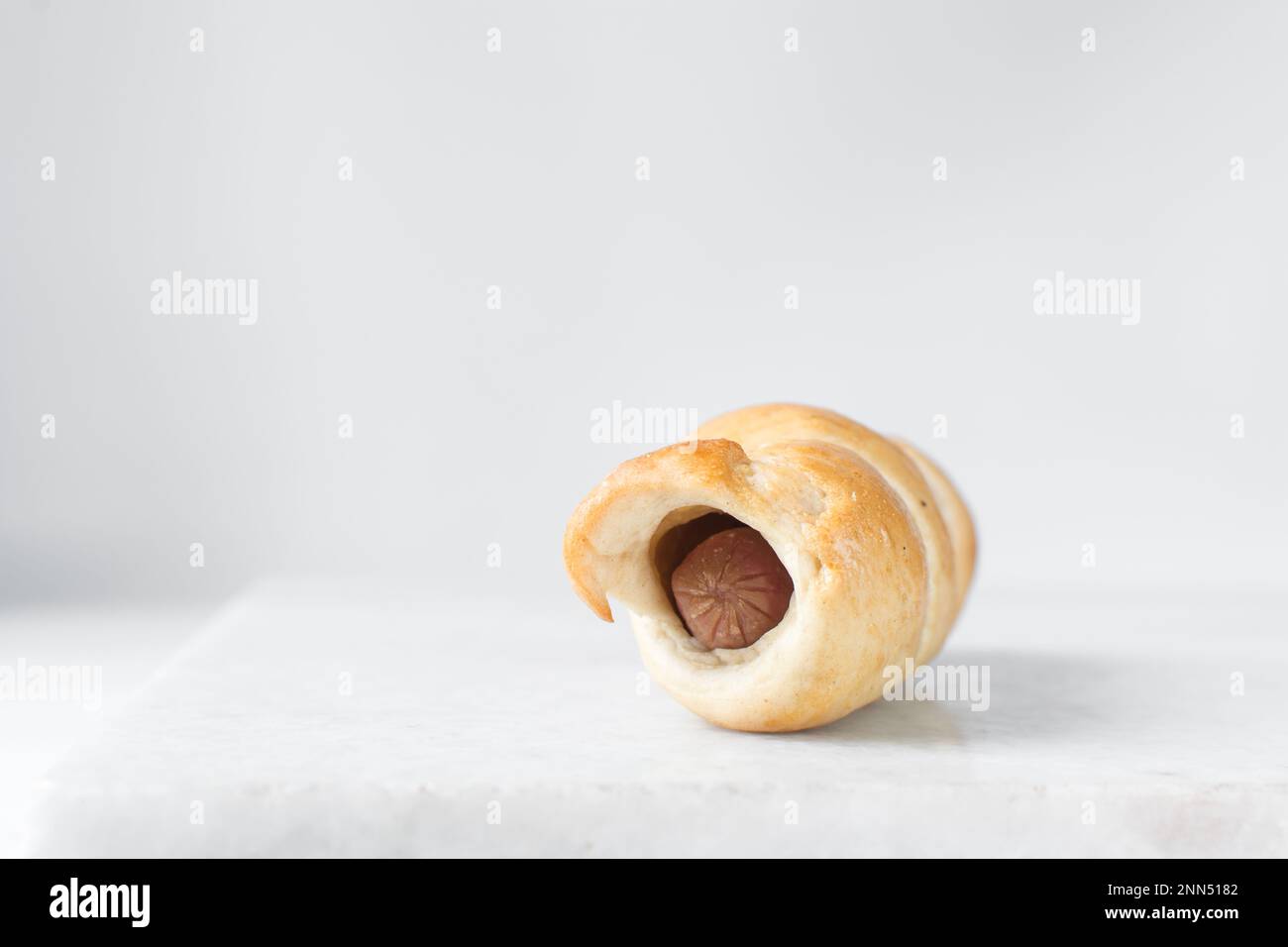 Würstchenrolle auf einem Marmortablett, gedrehte Würstchenrolle auf einem Marmortablett, große Schweine in einer Decke Stockfoto