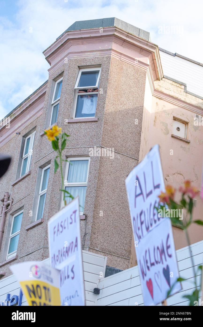 Ein Mensch beobachtet aus einem Fenster, wie sich die Antifaschisten aus Cornwall widersetzen, steht vor dem Beresford Hotel in Newquay, Cornwall, in dem Flüchtlinge untergebracht sind, während Demonstranten der rechtsextremen Gruppe Patriotic Alternative dagegen protestieren. Foto: Samstag, 25. Februar 2023. Stockfoto