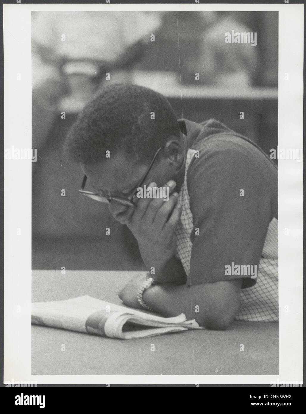Das Foto zeigt einen jungen afroamerikanischen Mann mit Brille, der sich über eine Zeitung lehnt, New York, NY, 8/1956. (Foto von Angelo Rizzuto Stockfoto