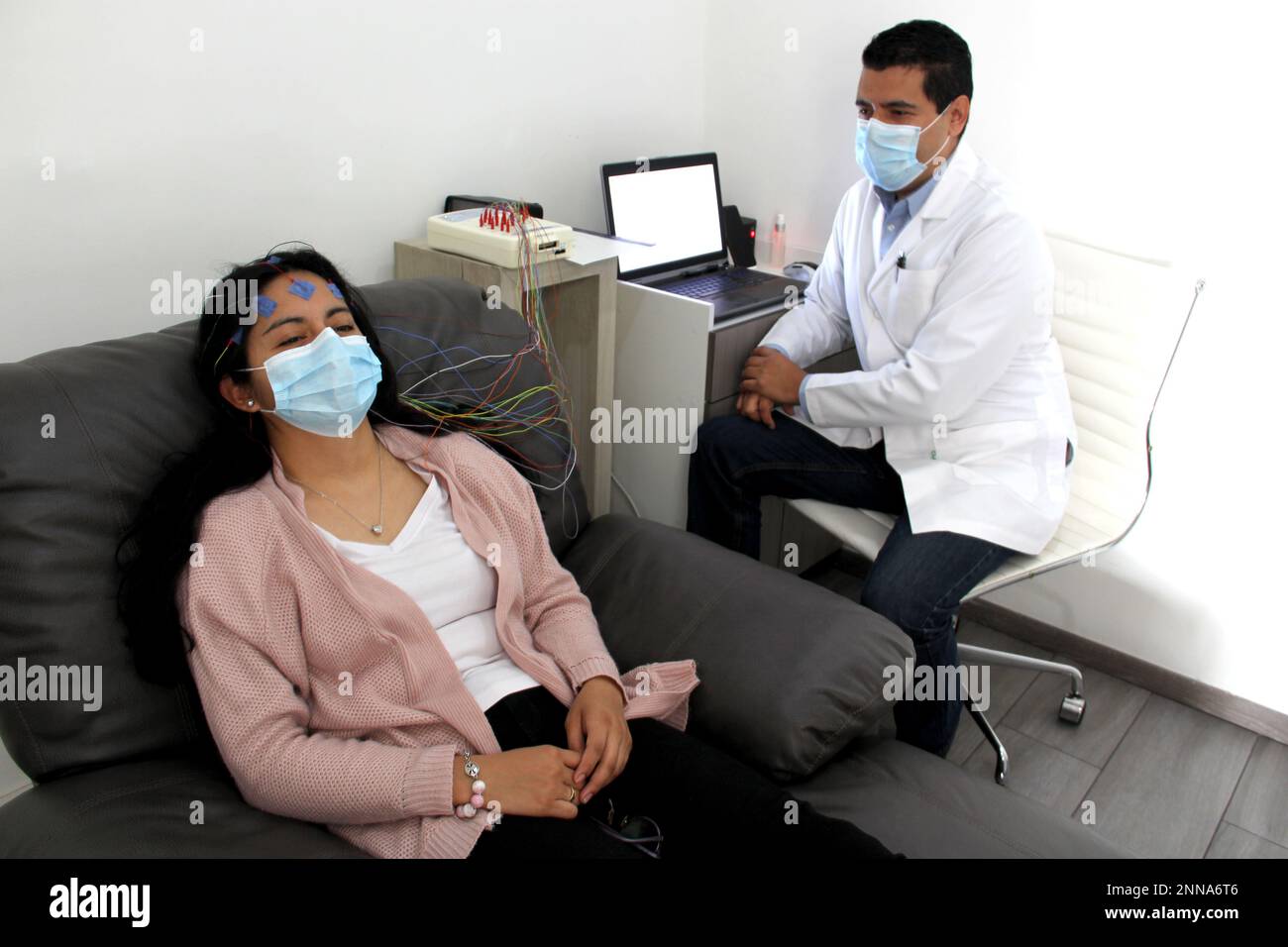 Lateinische Frau und Arzt mit Schutzmaske bei der Durchführung von Elektroenzephalogrammen und Hirnkartierung in Zeiten der Covid-19-Kontingenz Stockfoto