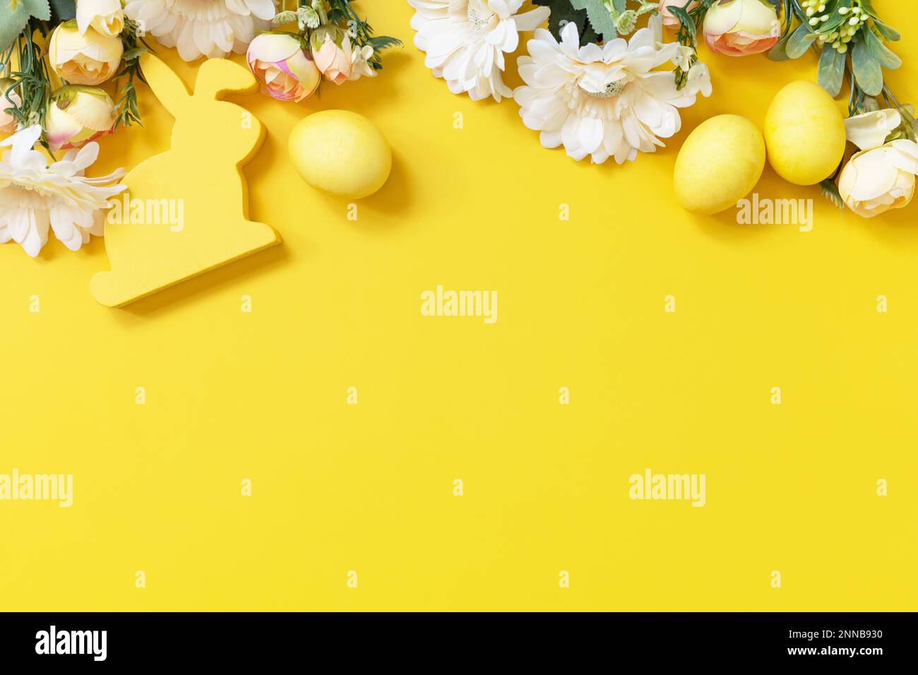 Ostergemisch mit bunten Eiern, Holzhasen und Frühlingsblumen auf gelbem Hintergrund. Blick von oben. Speicherplatz kopieren. Stockfoto
