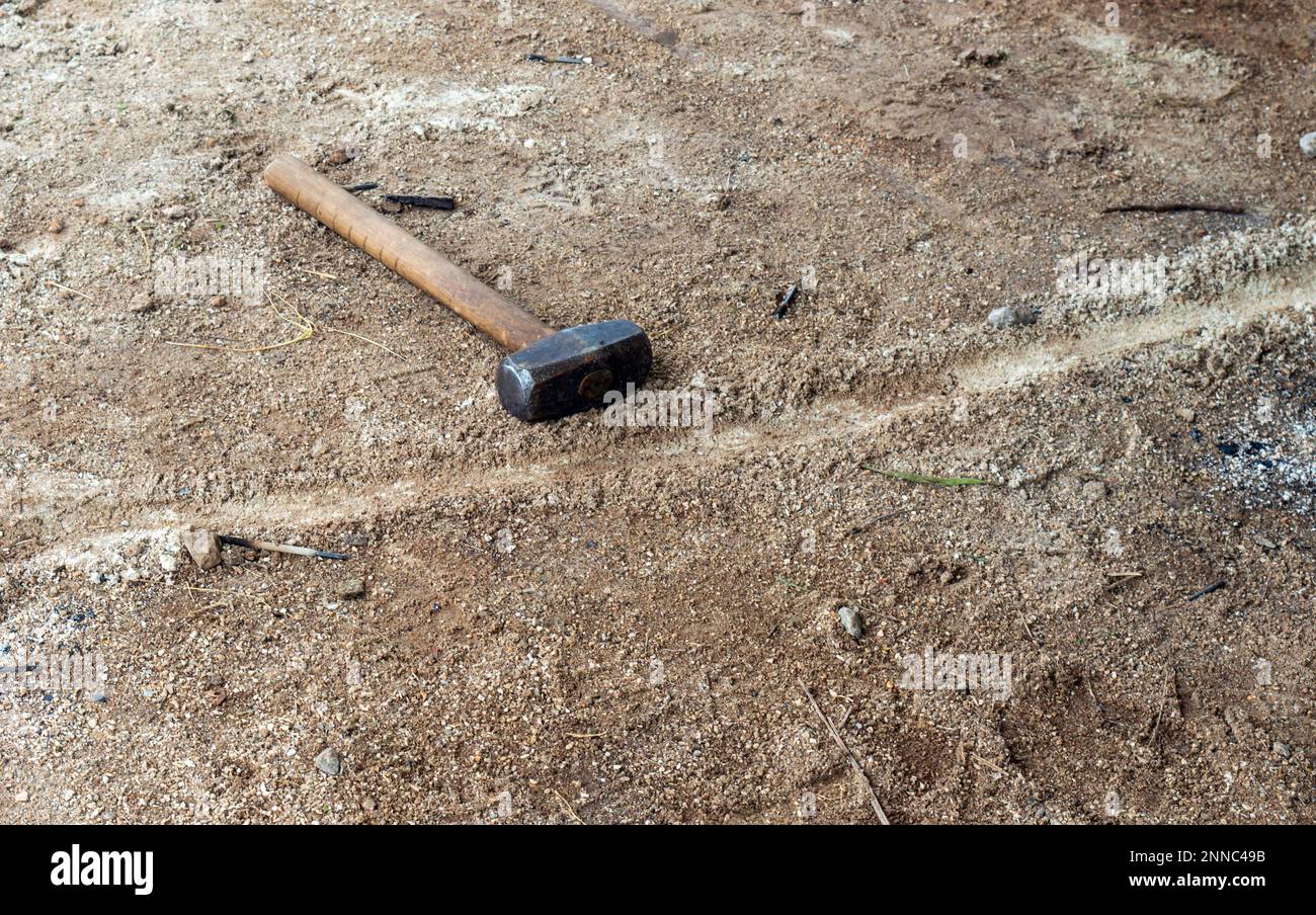 Der Handwerker hat seinen Vorschlaghammer auf dem trockenen, ausgetrockneten Boden liegen lassen. Das Werkzeug ist so konstruiert, dass es stumpfe Kraft auf einen Bereich oder ein Objekt ausübt. Stockfoto