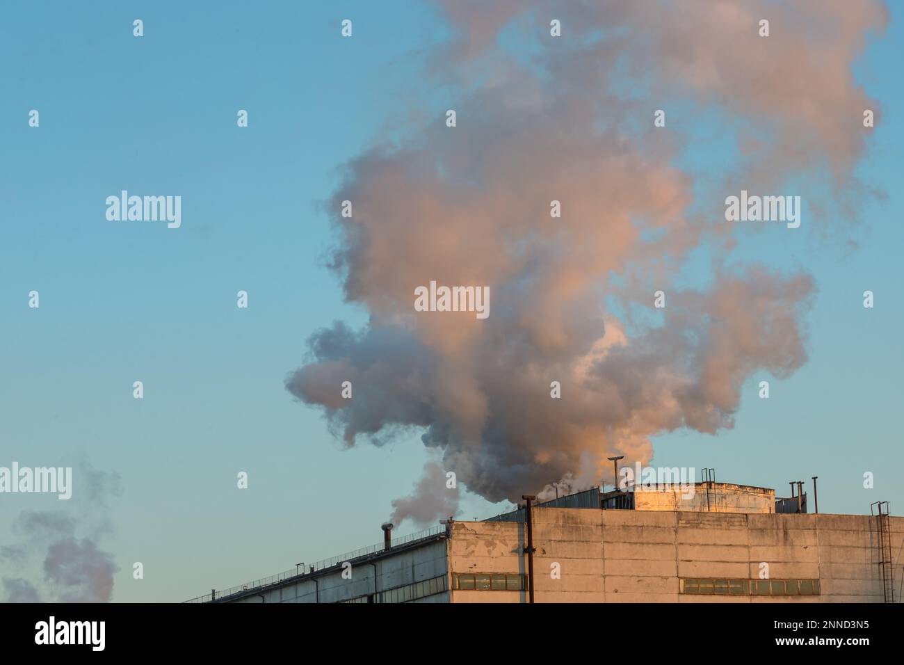 Ziegelschornstein mit weißem Rauch über einem Industriegebäude. Stockfoto