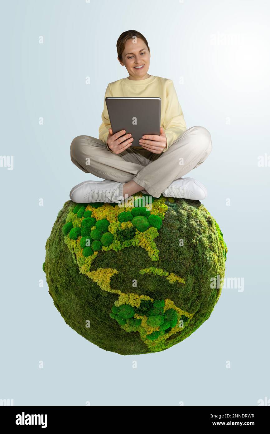Frau mit digitalem Tablet, die auf dem grünen Planeten Erde sitzt. Konzept der nachhaltigen Entwicklung und Umwelterziehung Stockfoto