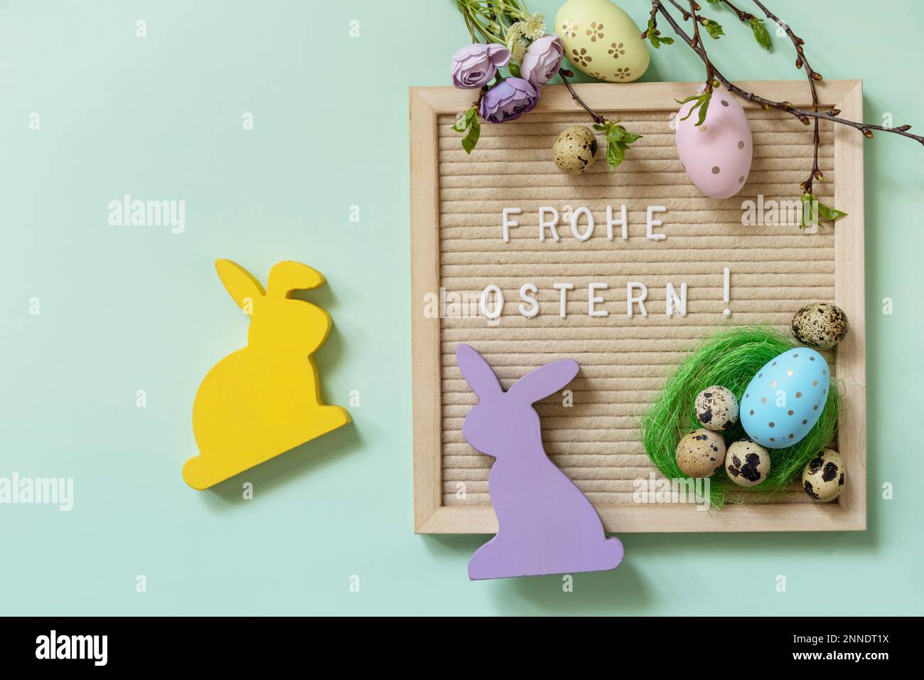 Brieftafel mit Frohe Ostern: Frohe Ostern in deutscher Begrüßung, Ostereier und grüne Zweige auf grünem Hintergrund. Blick von oben. Speicherplatz kopieren. Stockfoto