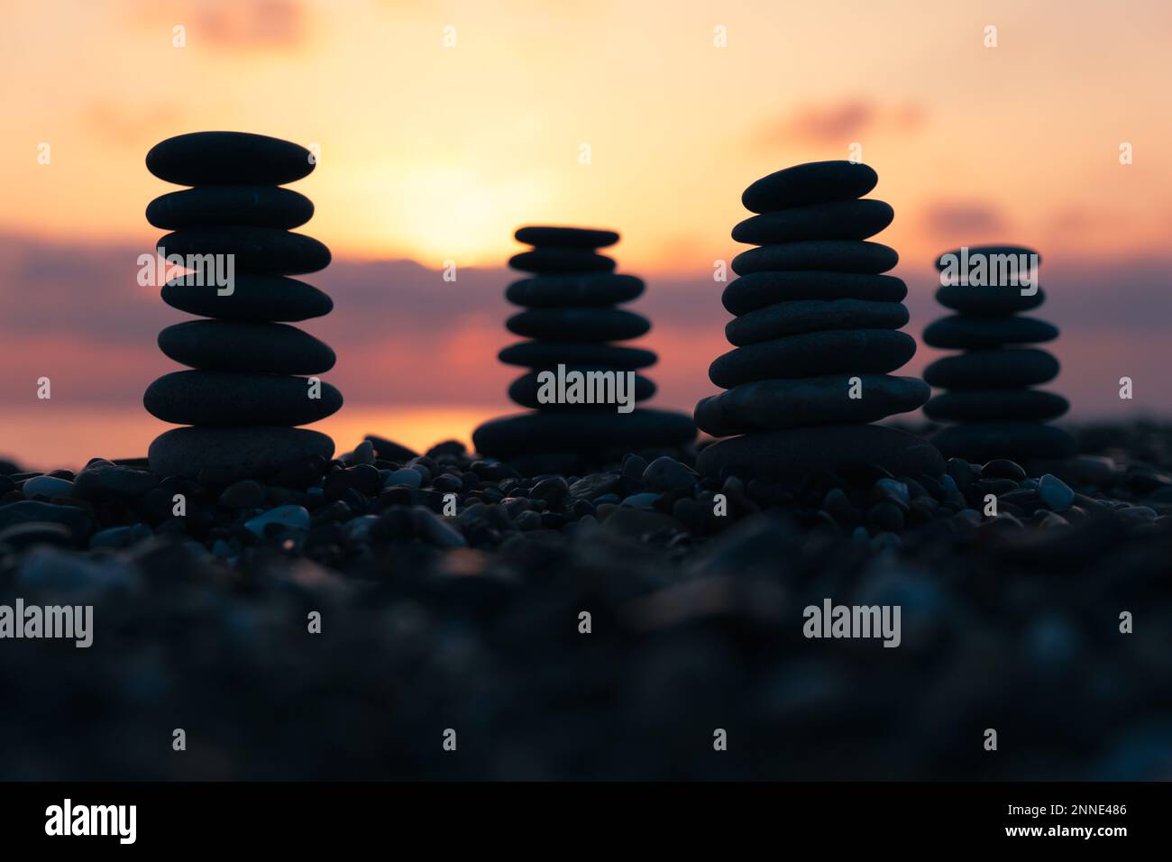 Ausgewogene Kieselpyramide am Strand bei Sonnenuntergang mit Meer im Hintergrund. Zen Steine am Strand, Meditation, Spa, Harmonie, Ruhe, Stockfoto