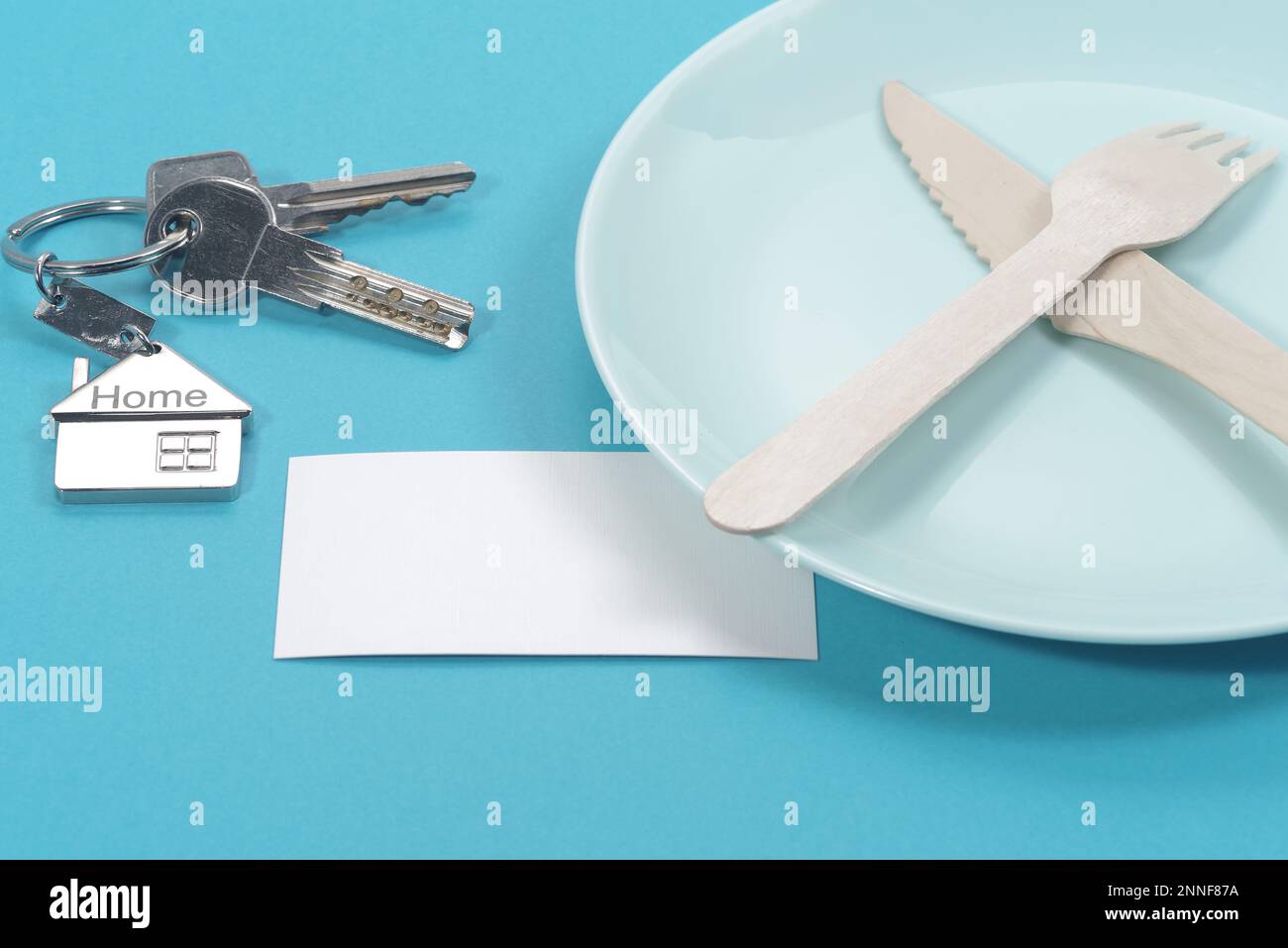 Haussymbol mit silbernen Schlüsseln und leerer weißer Visitenkarte auf blauem Hintergrund. Immobilienkonzept Stockfoto