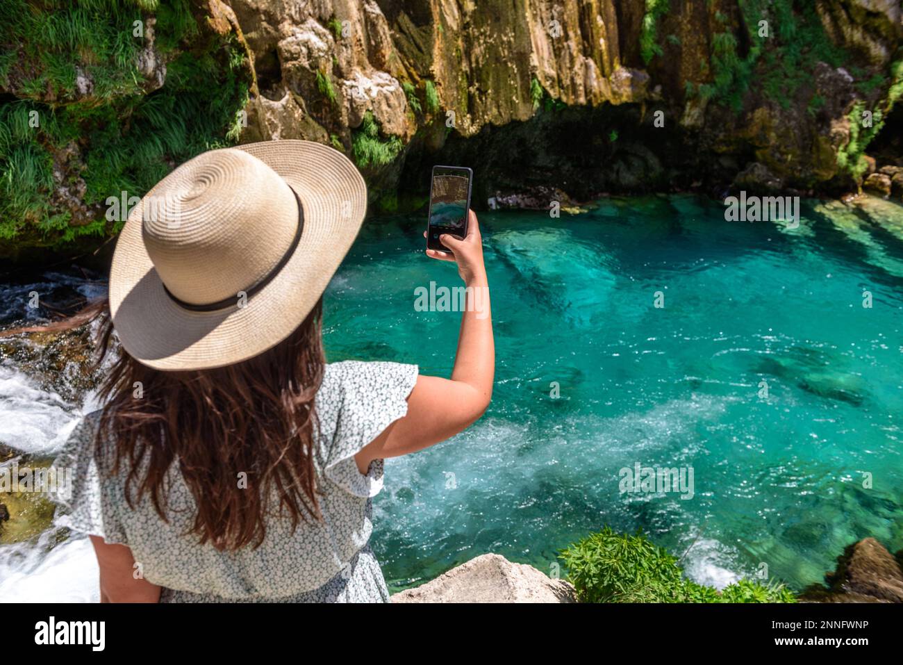 Rückansicht eines Mädchens, das ein Foto vom wunderschönen türkisfarbenen Bach unter den felsigen Klippen am Krcic Wasserfall in der Nähe von Knin, Kroatien, macht Stockfoto