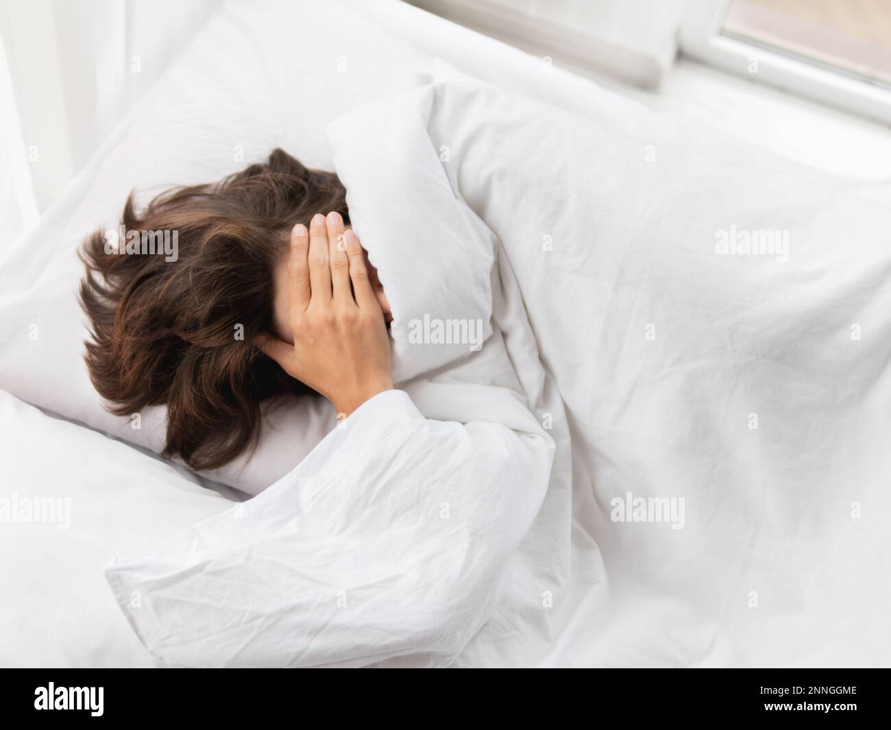 Schläfrige Frau mit Händen im Haar sitzt im Bett. Frau in Depressionen oder mit Kopfschmerzen. Stockfoto