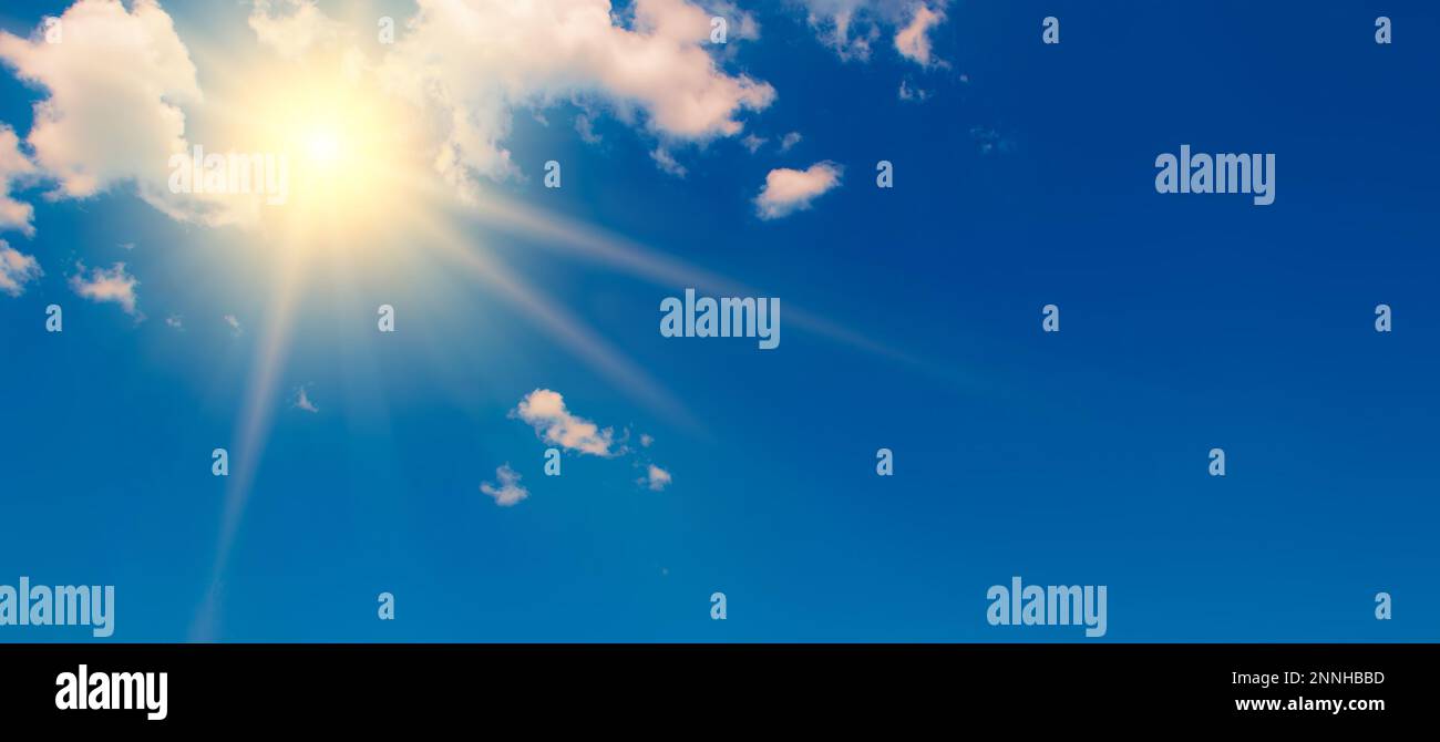 Blauer Himmel mit weißen, flauschigen Wolken und heller Sonne mit Strahlen. Stockfoto