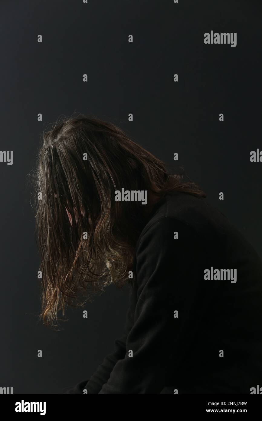 Porträt eines müden und depressiven Mannes mittleren Alters mit langen Haaren auf schwarzem Hintergrund. Depression, Angst, Phobie, Suizid und psychische Gesundheit. Stockfoto