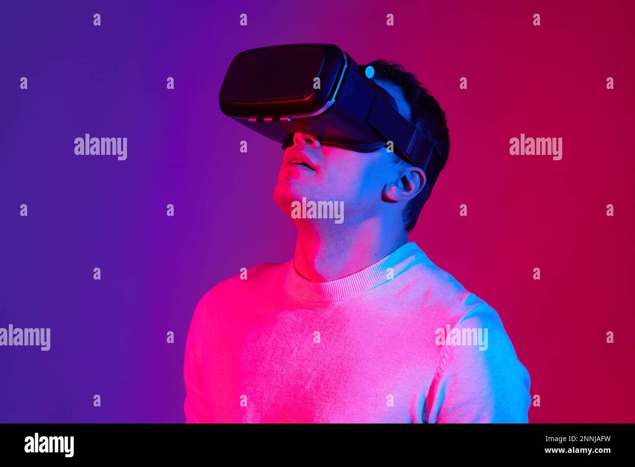 Ein junger Mann mit einem Virtual-Reality-Helm auf dem Kopf auf einem roten und blauen Hintergrund. Stockfoto