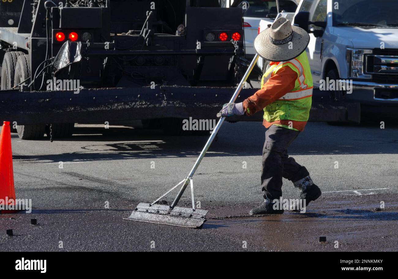 Straßenarbeiter, die Schutzkleidung und Stiefel tragen, glättet die Abdichtung von Frischschlamm Stockfoto