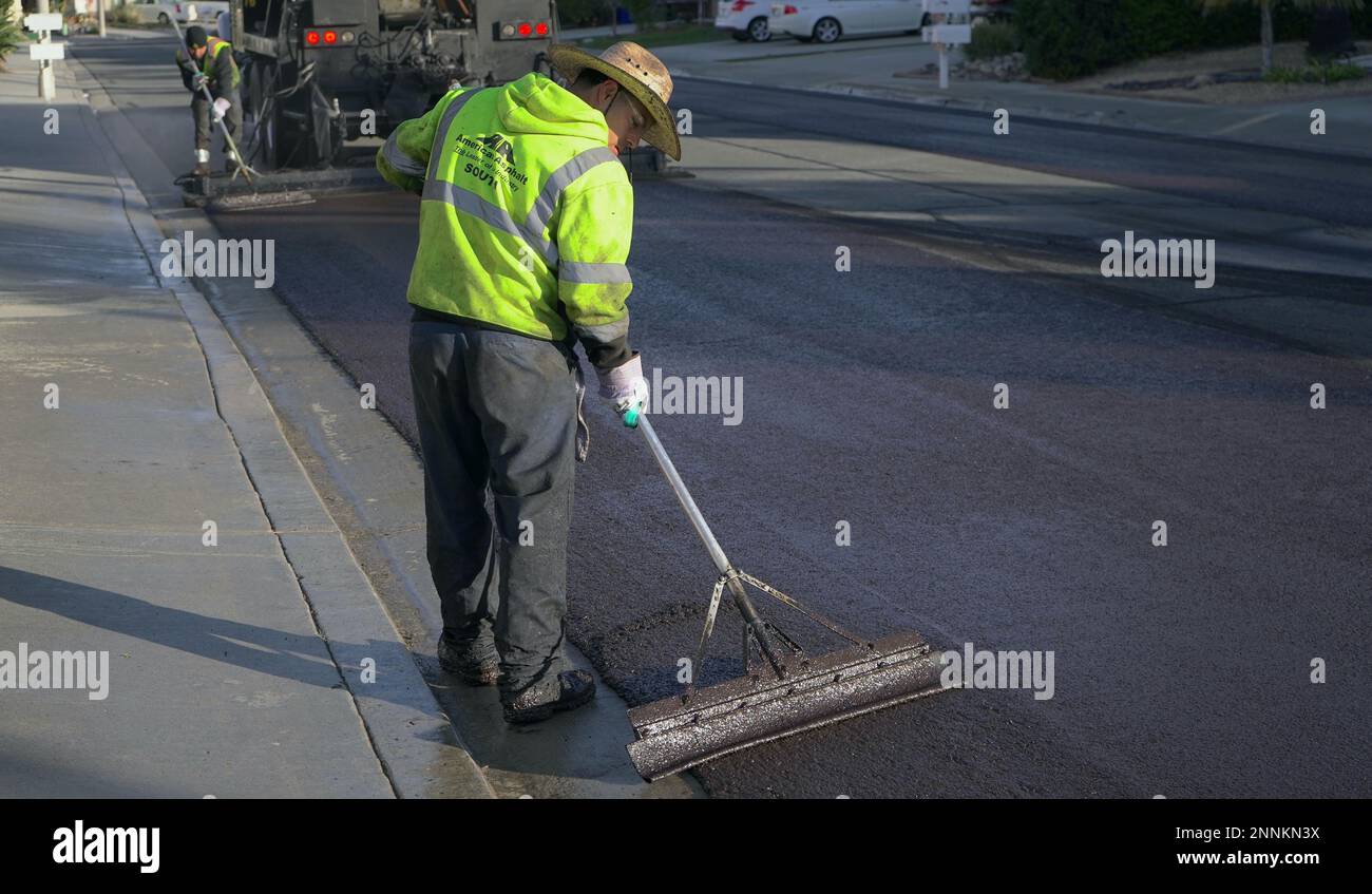 Straßenarbeiter, die Schutzkleidung und -Stiefel tragen, glättet die Abdichtung von Frischschlamm auf der Straße Stockfoto