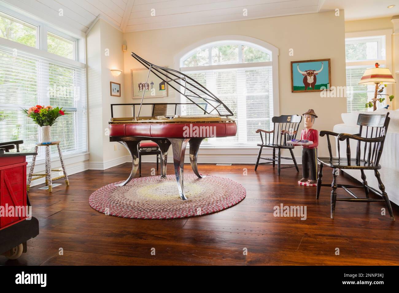 Klavier aus rotem Leder im Stil von Andreas Christensen aus Dänemark, schwarze Holzsessel und Folk Art Objekte im Wohnzimmer mit Eichenboden. Stockfoto