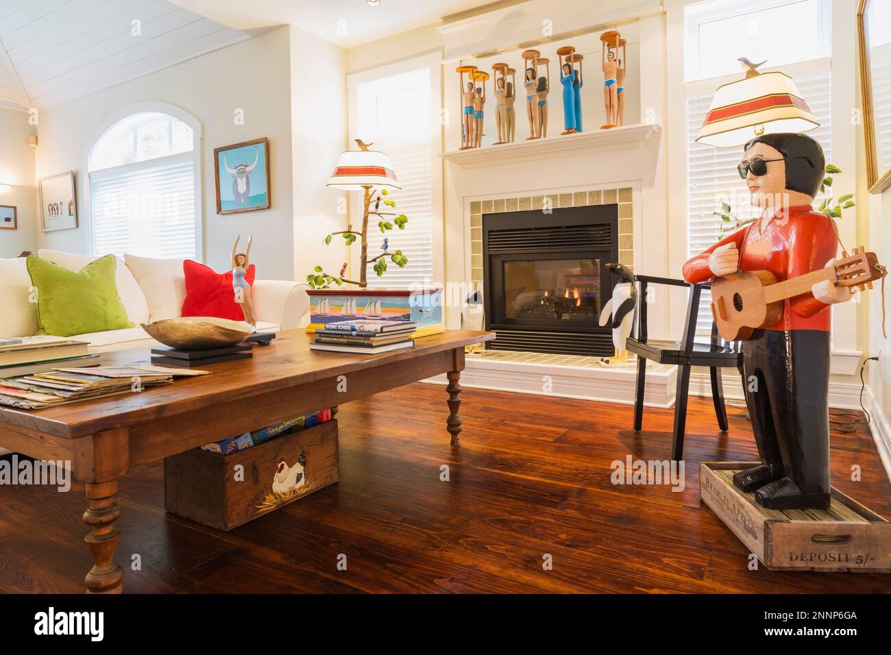 Couchtisch aus Kiefernholz im antiken Stil, weißes Polstersofa mit grünen und roten Velours-Kissen, Elvis Folk Art Skulptur, Kamin im Wohnzimmer. Stockfoto