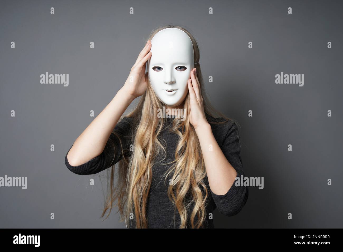 Geheimnisvolle junge Frau einstellen ihre Maske mit ihren Händen Stockfoto