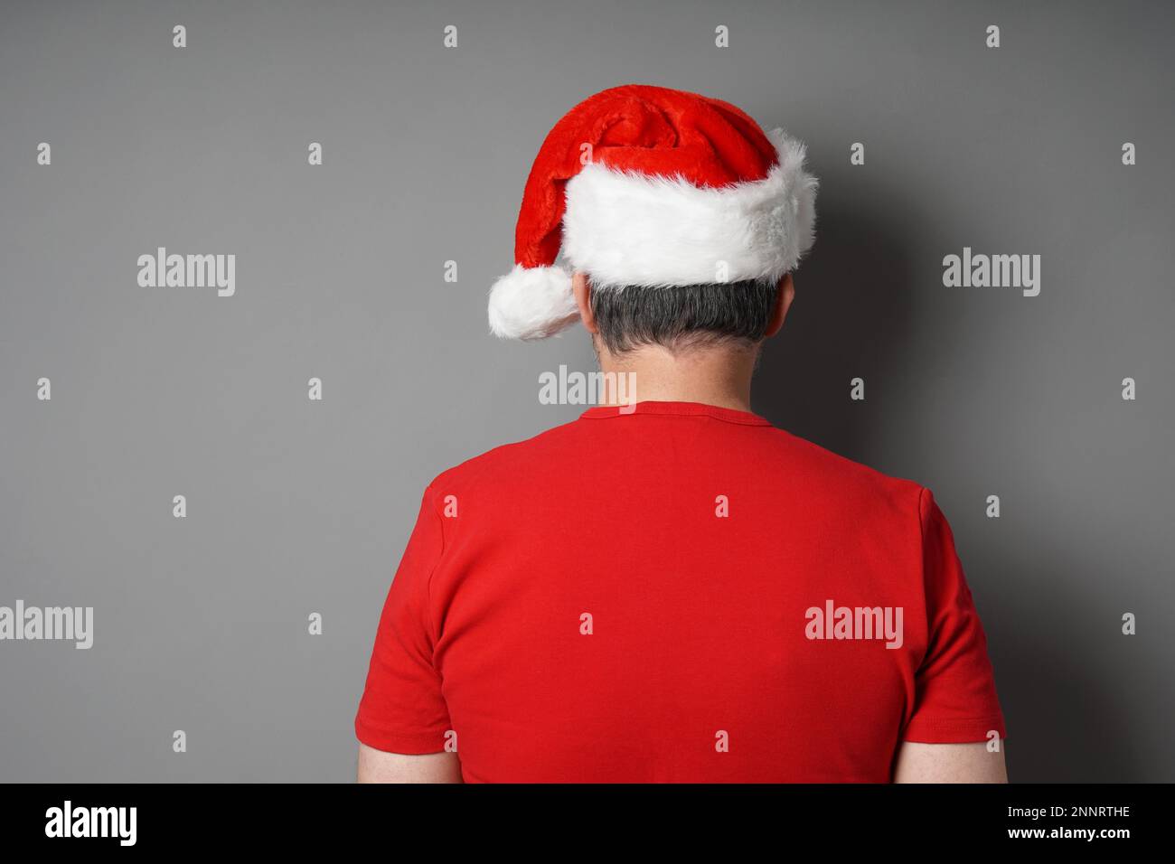 Ansicht der Rückseite des Mann, Santa Hat und Red-t-shirt gegen graue Wand Hintergrund mit Kopie Raum - echte Menschen Weihnachten Konzept Stockfoto