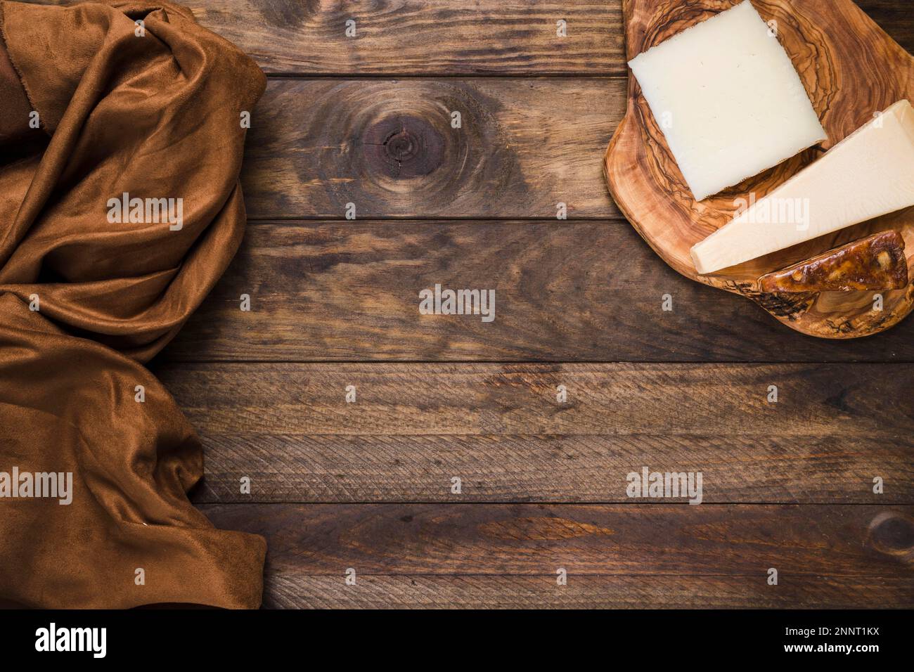 Leckere Käseplatte aus Holz mit braunem Seidenstoff und alter Holzoberfläche. Hochauflösendes Foto Stockfoto